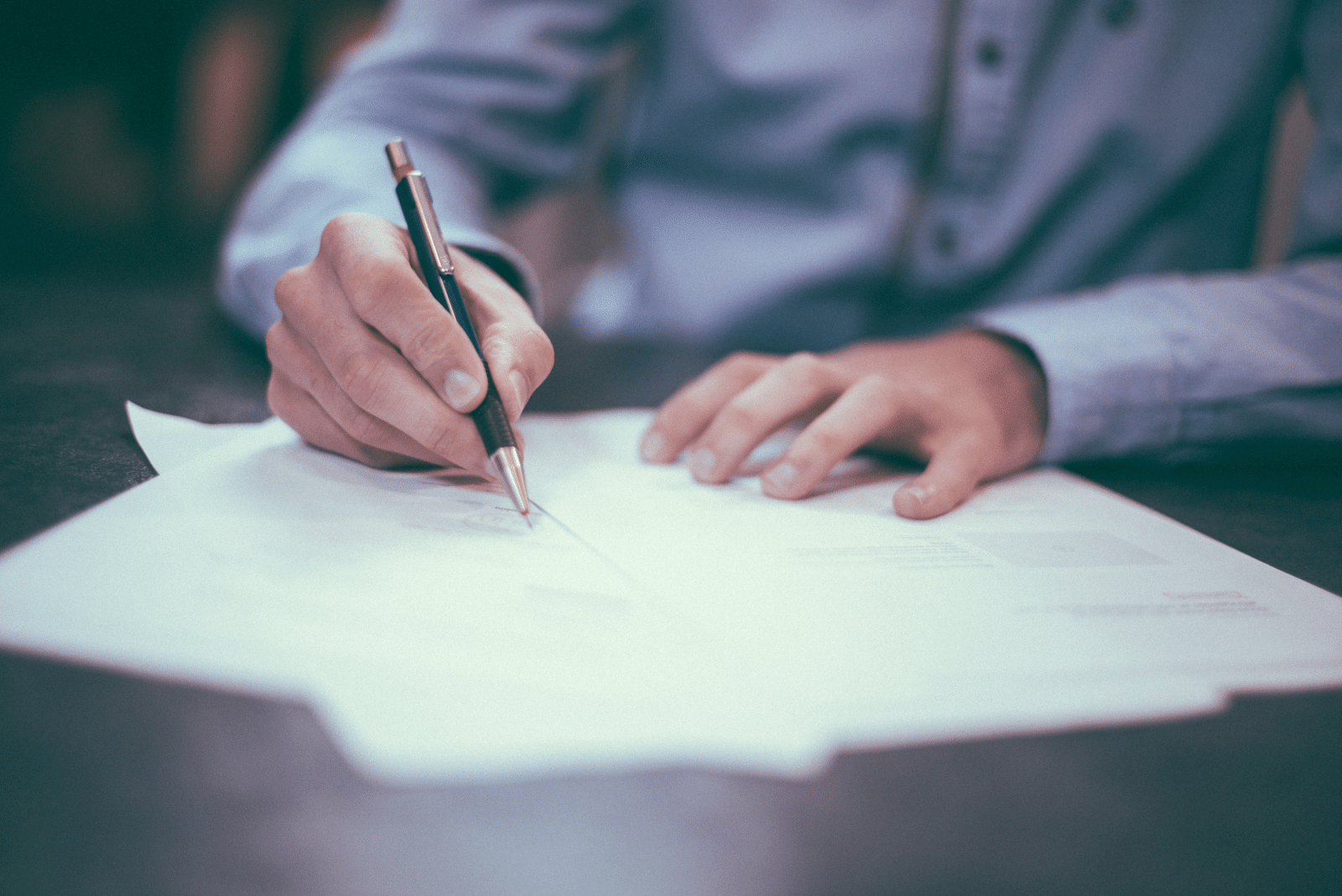 A picture of someone completing paperwork with a pen.